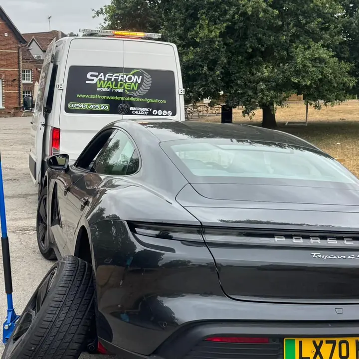 A Porsche Taycan with a wheel off outside a pub, the van behind it